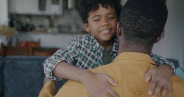 Yavaş çekimde, mutlu Afro-Amerikalı çocuğun, babasına sarılıp gülümseyen, kameraya bakıp dairede sevgisini ifade eden portresi. Çocukluk ve aile kavramı.