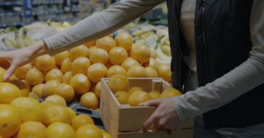 Perakende mağazasında çalışan kadın el tacirlerinin portakalları süpermarketin raflarına koyması. Organik meyve ve manav konsepti.