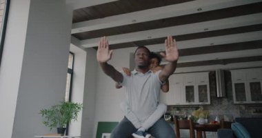 Afrikalı Amerikalı baba, küçük oğluyla birlikte dairede spor yaparken çömeliyor. Babalık ve aktif yaşam tarzı kavramı.