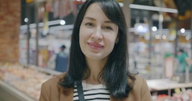 Modern süpermarkette kameraya gülümseyen mutlu genç bir kadının yavaş çekim portresi. Memnun bayan müşteri ve alışveriş konsepti.