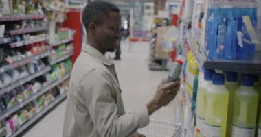 Afro-Amerikalı süpermarket müşterisi temizlik ürünleri seçiyor perakende mağazasından tramvay alışverişi yapıyor. Halk ve tüketim kavramı.