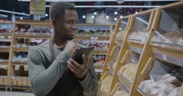 アフリカ系アメリカ人のセールスマンは スーパーマーケットで在庫を確認する棚の製品をチェックするタブレットを使用しています 人と小売ビジネスコンセプト — ストック動画