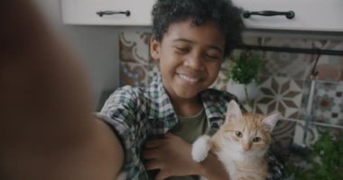 Afro-Amerikalı bir çocuğun portresi çevrimiçi video konuşması yaparken kedi yavrusunun evdeki kameraya baktığını gösteriyor. İletişim ve çocukluk kavramı.