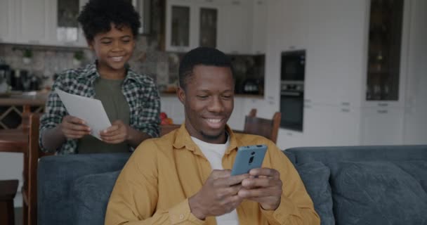ハッピーアフリカ系アメリカ人の男は 自宅のキッチンで父親の日に子供からパパギフトカードが大好きです 父性と愛する家族のコンセプト — ストック動画