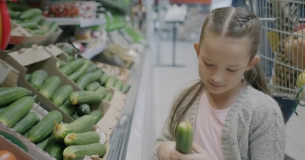 スーパーの野菜部門でキュウリを選択する小さな少女の愛らしい子供のゆっくりとした動き ショッピングと幸せな子供時代のコンセプト — ストック動画
