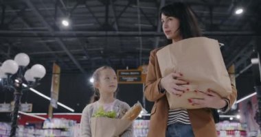 Anne ve çocuk ellerinde alışveriş torbalarıyla süpermarkette yürürken alışveriş hakkında konuşuyorlar. Tüketim ve aile yaşam tarzı kavramı.