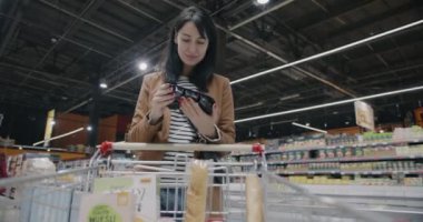 Gıda seçen genç kadın süpermarket perakende mağazasında alışveriş yapan tramvaya ürün koyuyor. Bakkaliye ve tüketim kavramı.