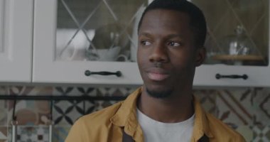Afrika kökenli Amerikalı bir adamın yavaş çekim portresi kameraya dönüyor ve evde mutfakta gülümsüyor. Halk ve iç mekan kavramı.