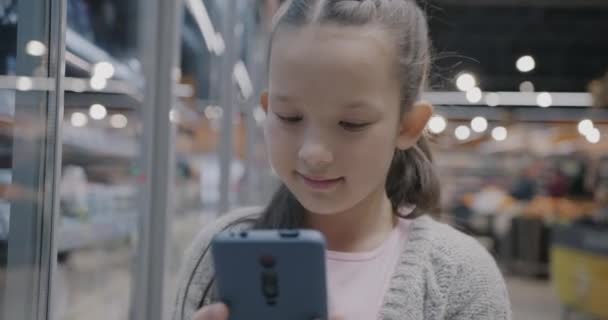 Söt Liten Flicka Med Hjälp Smartphone Pekskärm Stående Moderna Snabbköp — Stockvideo