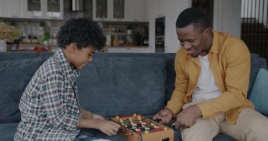 Mutlu Afrikalı Amerikalı baba ve oğul evde mutfakta langırt oynuyorlar. Masa futbolu ve çocukluk aktivitesi konsepti.