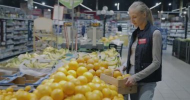 Kadın süpermarket çalışanı taze organik portakalları satıp müşteriler için meyve hazırlıyor. Perakende ve manav konsepti.