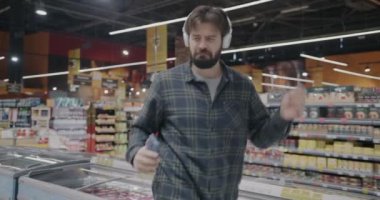 Süpermarkette dans eden kulaklık takan adam akıllı telefon tutarak eğleniyor. Modern yaşam tarzı ve olumlu duygu kavramı.