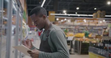 Afro-Amerikalı süpermarket çalışanı yemek kontrolü için envanter yazıyor. Perakende ticaret ve tüketim kavramı.
