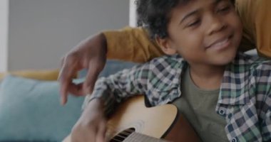 Sevgi dolu babasıyla gitar çalan sevimli Afro-Amerikalı çocuğun yakın çekimi evde yaratıcı aktivitelerin keyfini çıkarıyor. Mutlu çocukluk ve müzik konsepti.