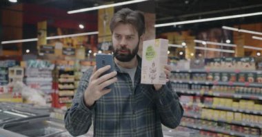 Genç adam internetten yiyecek ürünlerinin süpermarkette akıllı telefon kullanarak alışverişi tartıştığını gösteriyor. Modern teknoloji ve alışveriş kavramı.