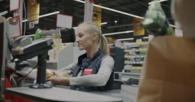 Kadın kasiyer gıda ürünlerini tarıyor ve süpermarketteki kasada kağıt torba içinde müşteriye veriyor. Alışveriş ve perakende satış konsepti.