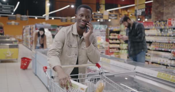 非洲裔美国人在手机上讨论在超级市场购买手推车的问题 通信和消费主义概念 — 图库视频影像