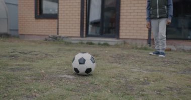 Çimenlikte koşan ve tek başına futbol oynayan bir çocuğun düşük açılı çekimi. Çocukluk ve aktif yaşam tarzı kavramı.