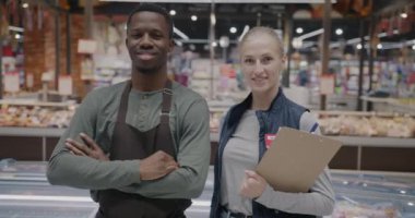 Mağazada durup kameraya gülümseyen kadın ve erkek süpermarket çalışanlarının yavaş çekim portresi. İnsanlar ve perakende sektörü kavramı.