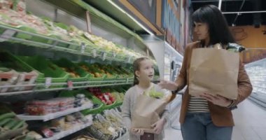 Anne ve kızının süpermarkette ellerinde kese kâğıdıyla dolaşarak birlikte alışverişe çıkmaları. Aile yaşam tarzı ve market konsepti.