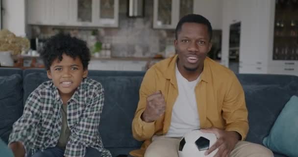 父親と息子の肖像画は アフリカ系アメリカ人がテレビでサッカーを見ているのを楽しませてくれました スポーツと家族のライフスタイルのコンセプト — ストック動画