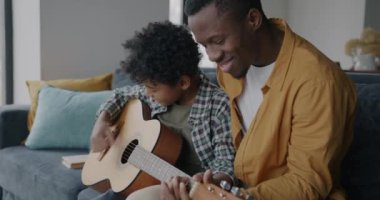 Sevimli küçük çocuk ve yetişkin erkek baba birlikte gitar çalıyor müziğin ve aile hayatının tadını çıkarıyor. Mutlu çocukluk ve babalık kavramı.