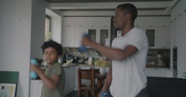 Küçük çocuk ve yetişkin adam baba halterlerle antrenman yapıyor apartmanda spor yapıyor, gülümsüyor. Aktif yaşam tarzı ve sağlıklı çocuk konsepti.