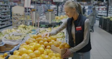 Portakalları rafa koyan kadın çalışan süpermarkette çalışıyor ve meyveleri satışa hazırlıyor. Perakende ve market konsepti.