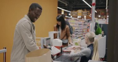 Afro-Amerikalı bir adam süpermarketten yiyecek alıyor kağıt torba içinde alışveriş yapıyor kasiyere gülümsüyor. İnsanlar ve perakende sektörü kavramı.