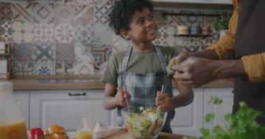 Afro-Amerikalı bir adam evde güzel bir çocukla salata pişiriyor ve evde yemek hazırlıyor. Aile hayatı ve baba oğul ilişkisi kavramı..