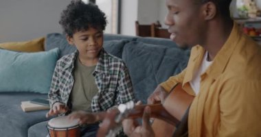 Baba yetişkin bir adam evde gitar çalarken tatlı Afro-Amerikan çocuk davul çalıyor. Aile ilişkisi ve gençlik kültürü kavramı.