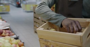 Erkek eli elmalarını tahta kutuya koyarken pazarlamacı da markette meyve topluyor. Perakende mağazası ve gıda konsepti.
