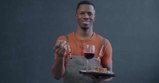 アフリカ系アメリカ人ウェイターの笑顔のゆっくりとした動きの肖像画は グレーの背景で支払うことを求める手のジェスチャーを作る食べ物を保持しています お金とケータリングビジネスコンセプト — ストック動画