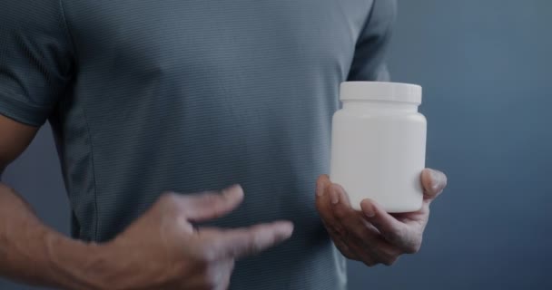 アフリカ系アメリカ人スポーツマンがサプリメントを宣伝しながら マルチビタミンの瓶を指す男性の手のクローズアップ 健康的な栄養とスポーツのコンセプト — ストック動画