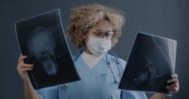 身着制服的非洲裔美国女医生的画像 在灰色背景下看着人类头骨的X光图像 医药和保健概念 — 图库视频影像