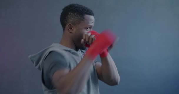 スポーツをするプロのアフリカ系アメリカ人のボクサーの肖像画 紫色の背景に包まれた手で空気を打つ練習に集中 — ストック動画