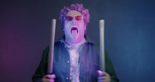 用霓虹灯棒玩乐的家伙在充满活力的紫色背景下做出滑稽的脸的慢动作肖像 创造力和人的概念 — 图库视频影像