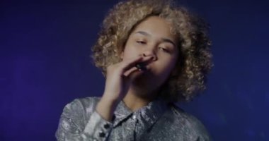 Mavi arka planda dans eden ve elektronik sigara içen mutlu Afrikalı Amerikalı kadın portresi. Modern yaşam tarzı ve vape konsepti.