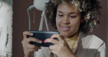 Neşeli Afro-Amerikalı kadın, internet üzerinden video oyunu oynuyor. Akıllı telefon iş arasında ofiste dinleniyor. Eğlence ve oyun aygıtı konsepti.