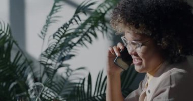 Neşeli Afrikalı Amerikalı girişimci cep telefonuyla konuşma yaparak günışığı ofisindeki modern akıllı telefonu kullanarak işi tartışıyor. İletişim ve iş konsepti.