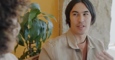 Neşeli Asyalı adam, içeride konuşmaktan keyif alan, gülümseyen Afrikalı Amerikalı bir kadınla konuşuyor. İnsanlar ve iletişim konsepti.