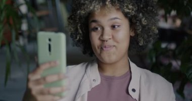 Neşeli Afrikalı Amerikalı öğrenci kampüsteki akıllı telefonuyla çevrimiçi video görüşmesi sırasında el sallayarak gülüyor. İnternet iletişimi ve insan kavramı.