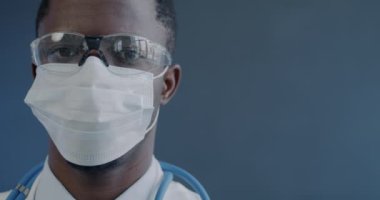 Üniformalı yüz maskesi takan ve gri arka planda kameraya bakan erkek doktorların yakın çekimi. Sağlık ve Tıp Konsepti.
