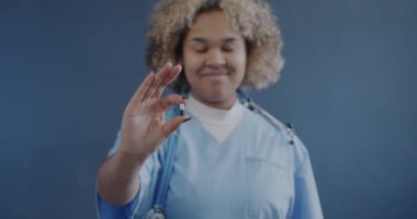 Kapsül tutan Afrikalı Amerikalı doktorun mavi arka plandaki kameraya gülümseyen portresi. İlaç ve eczane kavramı.