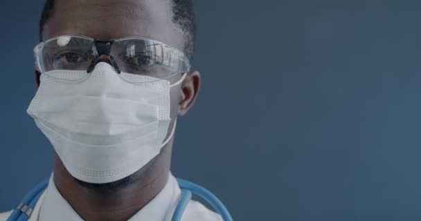 Nærbilde Mannlig Lege Med Uniform Ansiktsmaske Briller Som Ser Kamera – stockvideo