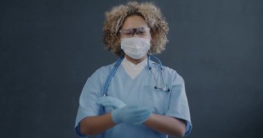 Üniformalı yüz maskesi takan ve kollarını kavuşturup mor arka planda kameraya bakan Afrikalı Amerikalı doktorların yavaş çekimleri.