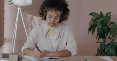 Kendine güvenen Afro-Amerikan bir kadının iş fikirlerini not defterine yazıp ofis odasındaki kameraya bakışının portresi. Girişimci ve profesyonel kalkınma kavramı.