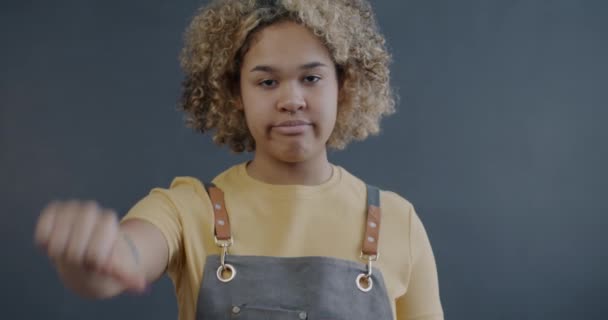 穿着围裙咖啡店的不快乐的非洲裔美国女士的慢动作肖像 在灰色背景下显示出大拇指朝下的手势 企业家和负面情绪概念 — 图库视频影像