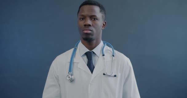 アフリカ系アメリカ人の医師のゆっくりとした動きの肖像画は カメラを見て灰色の背景に微笑んでいます 医学と医療のコンセプト — ストック動画