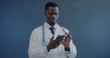 Doktorun hastaya danışmanlık yaparken akıllı telefon kullanan Afro-Amerikan üniformalı bir adamın portresi. Mobil bağlantı ve sağlık hizmeti kavramı.